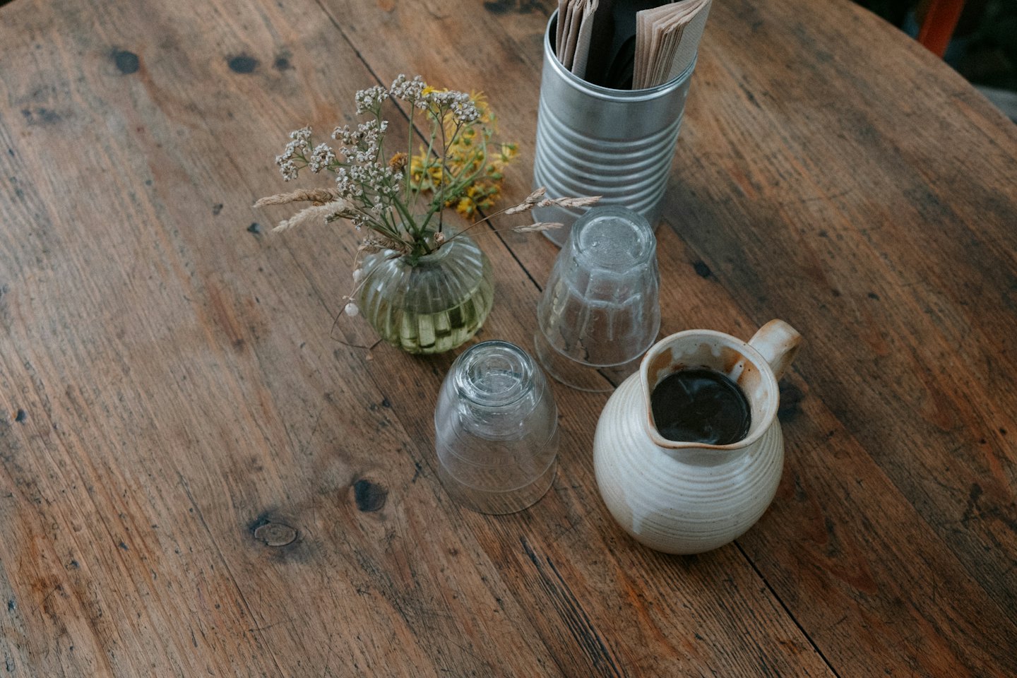 Tabletop arrangement featuring a ceramic pitcher, glassware, and rustic cutlery.